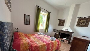 Um quarto com cama, poltrona, lareira e janela com cortinas.