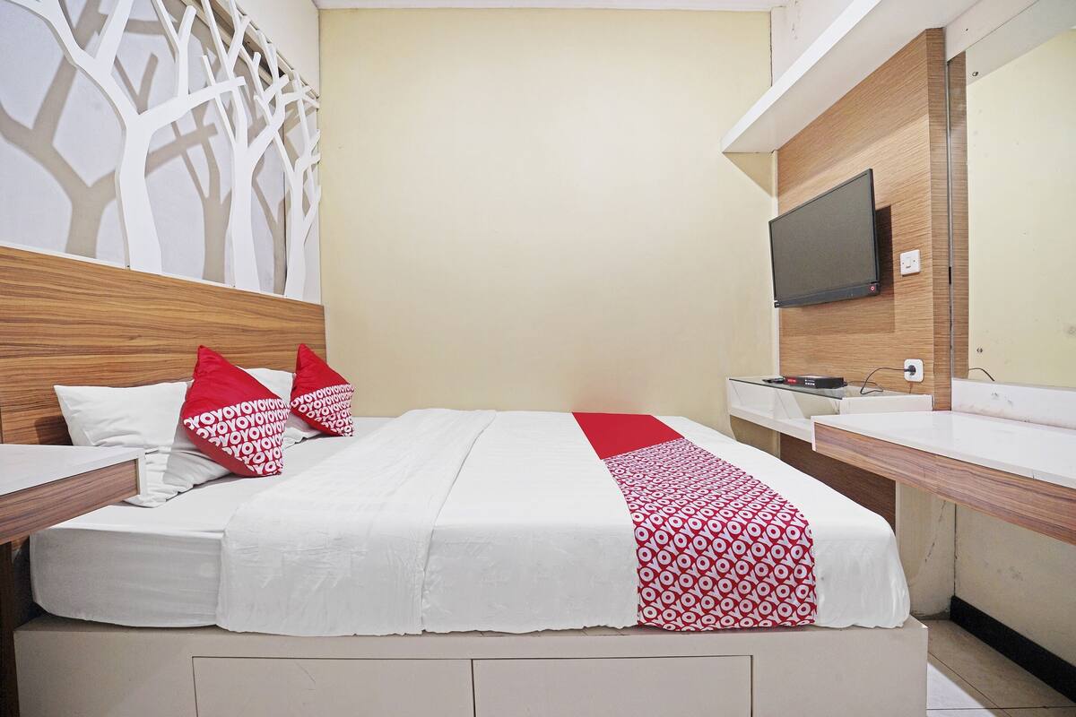A hotel room with a bed, a TV mounted on the wall, and a wooden headboard.