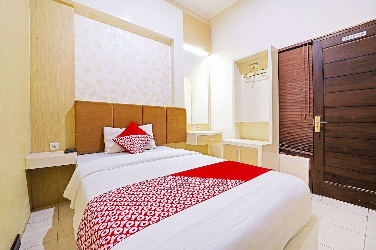 A hotel room with a large bed, a wooden headboard, a bedside table, a mirror, and a wardrobe.