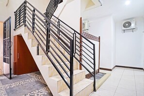 Eine Treppe mit schwarzen Geländern und beigefarbenen Stufen, die zu einem Raum mit weißen Wänden und Fliesenboden führt.