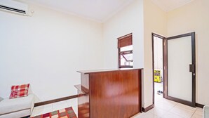 A hotel room with a wooden reception desk, a bed with a red and white patterned pillow, a window with blinds, and a tiled floor. - OYO 91342 Tatti Inn Syariah (Depok)