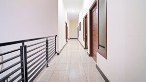 A hallway with a black metal railing, tiled floor, and wooden doors. - OYO 91342 Tatti Inn Syariah (Depok)