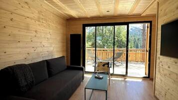 L’intérieur d’une cabane en bois, avec un canapé, une table basse et une porte-fenêtre coulissante donnant sur une terrasse extérieure.
