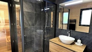 A modern bathroom with a glass-enclosed shower, a wooden vanity with a white sink, and a large mirror.