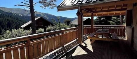 A wooden deck with benches and a pergola, overlooking a forested mountain area.