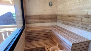 A sauna with wooden benches, a small bucket, and a window.