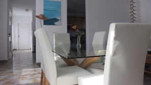 Een eetruimte met een tafel met glazen blad, witte stoelen en een schilderij aan de muur.