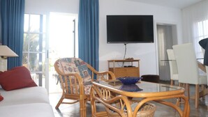 Een woonkamer met een bank, een fauteuil met patroon, een glazen salontafel en een flatscreen televisie aan de muur.