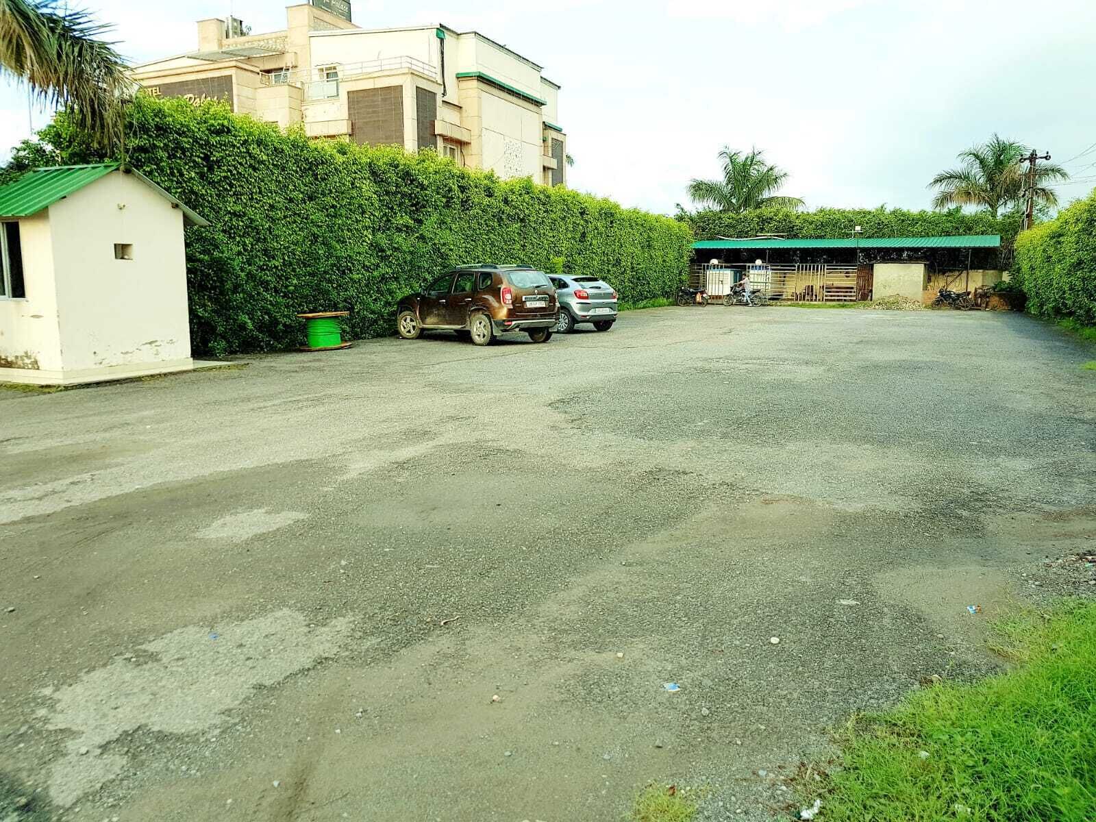 Un estacionamiento con dos coches, un bote de basura verde y un pequeño edificio blanco.