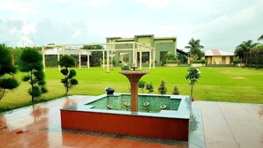 A courtyard with a fountain, a pergola, and a building in the background. - Hotel Riya Palace (Haldwani)