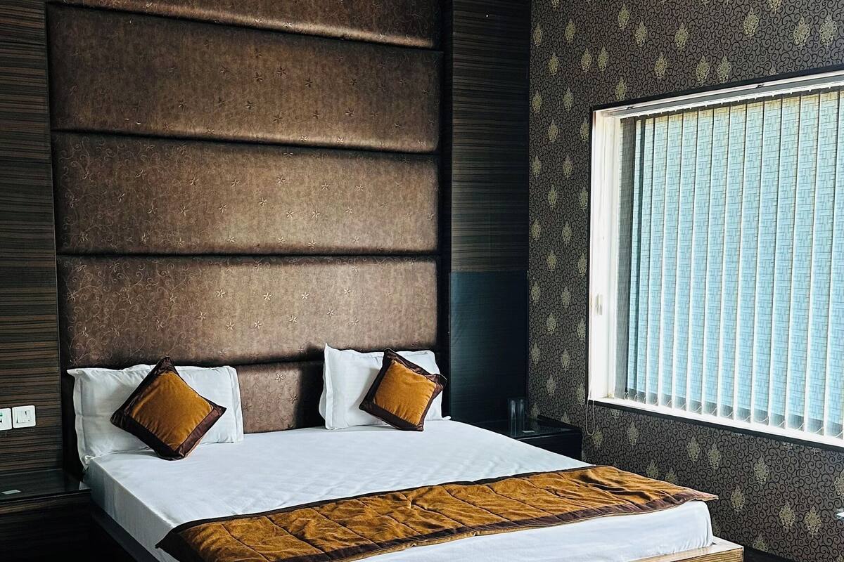 A modern bedroom with a large bed, dark patterned walls, and a window with blinds.