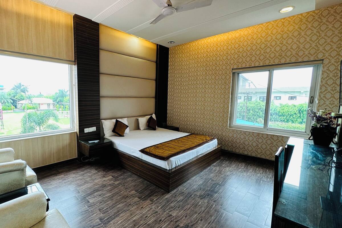 A modern hotel room with a large bed, two bedside tables, a chair, and large windows offering a view of the outdoors.