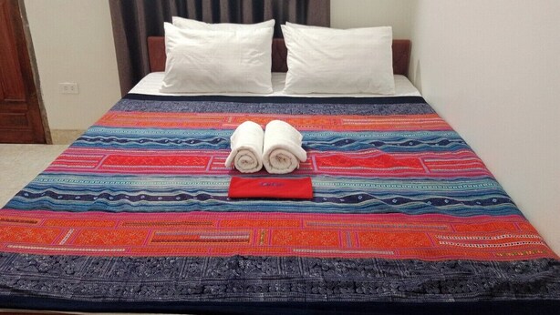 A bed with a colorful bedspread, two rolled towels, and a red object on the bed. - Ha Giang Yolo House and Loop Tours (Ha Giang 1)