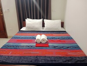 A bed with a colorful bedspread, two rolled towels, and a red object on the bed. - Ha Giang Yolo House and Loop Tours (Ha Giang 1)