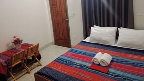 A bedroom with a bed, a wooden chair, a small table with a vase, and a door. - Ha Giang Yolo House and Loop Tours (Ha Giang 1)