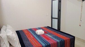 A single bed with a colorful blanket and a rolled towel, a white pillow, and a wall-mounted fan. - Ha Giang Yolo House and Loop Tours (Ha Giang 1)