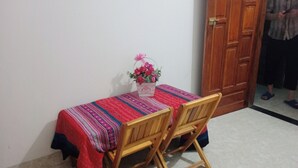 A small dining area with a table covered by a colorful tablecloth, two wooden chairs, and a basket with flowers. - Ha Giang Yolo House and Loop Tours (Ha Giang 1)