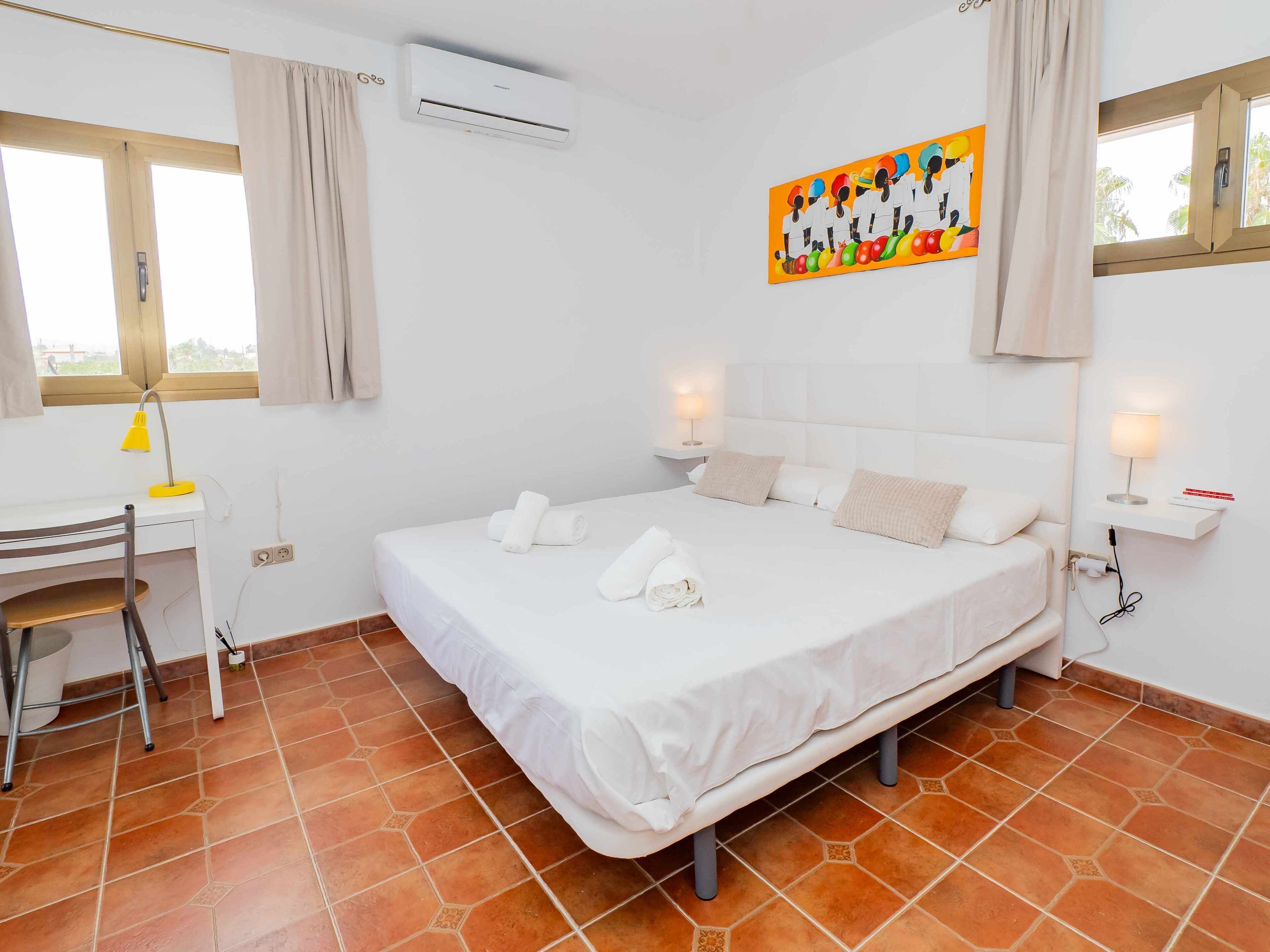 Une chambre d’hôtel avec un lit, un bureau, une chaise, un climatiseur et un tableau au mur.