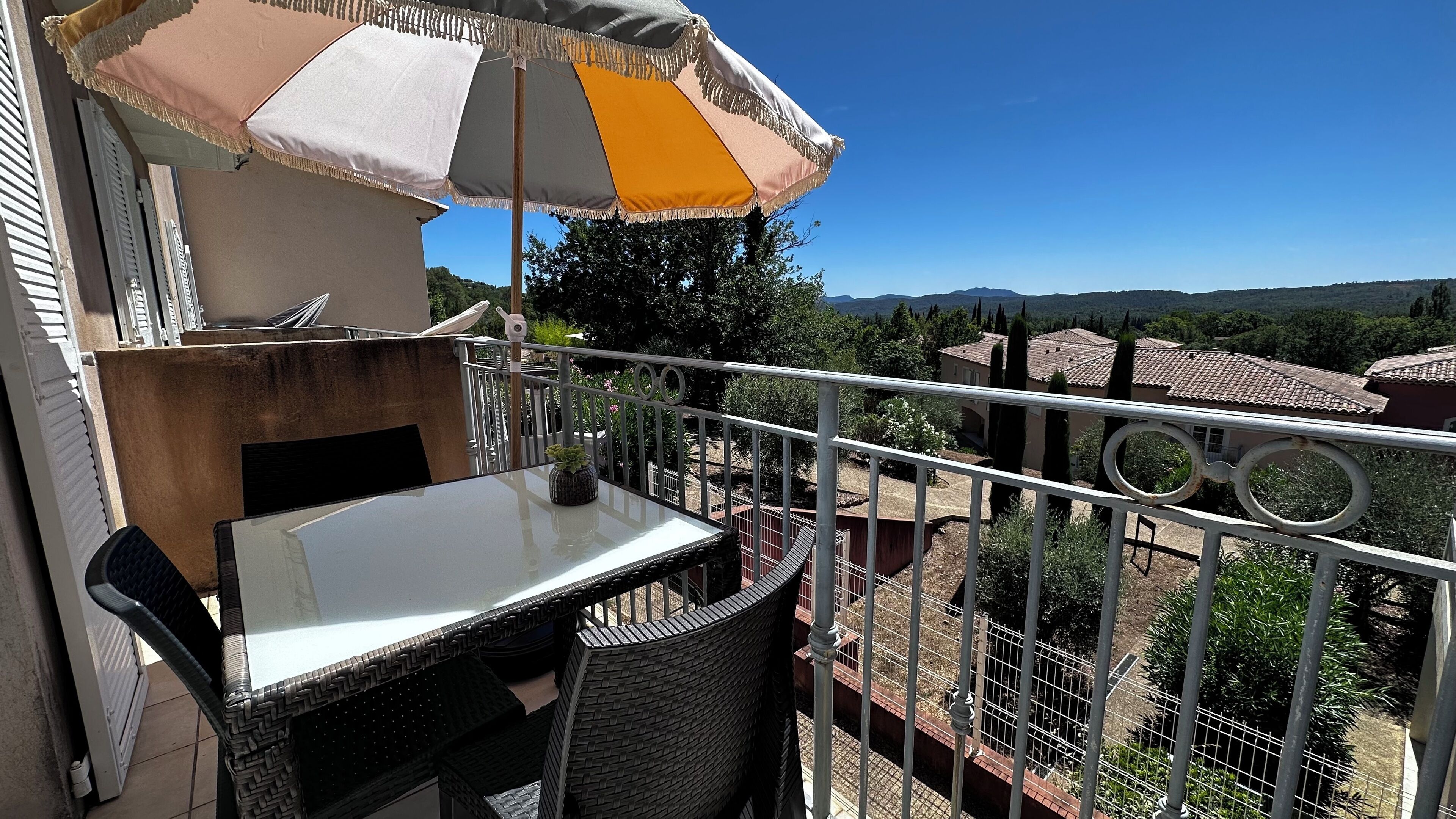 Un balcone con tavolo e sedie, un ombrellone e vista sul paesaggio circostante.
