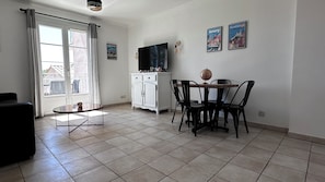 A living room with a dining area, a TV on a cabinet, and two framed pictures on the wall.