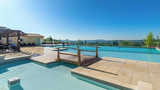 Un espace piscine doté d’une terrasse en bois, de chaises longues et offrant une vue sur les montagnes.