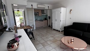 Une cuisine moderne avec des meubles blancs, un coin repas doté d’une table et de chaises en bois, et un canapé noir dans l’espace salon.