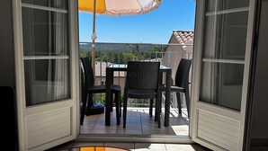 Un balcon ouvert avec un parasol jaune, des fauteuils en osier et une vue sur le paysage.