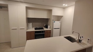 A compact kitchen with white cabinets, a built-in oven, a sink, and a refrigerator. - Modern 1-bedroom Unit in Dicksonnear Shops (Dickson)