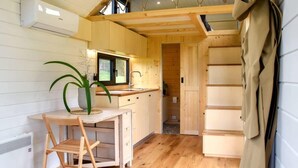 A compact kitchen with wooden cabinets, a dining table, and a potted plant. - Böstebacken Tiny House by Tiny Away (Alingsås)