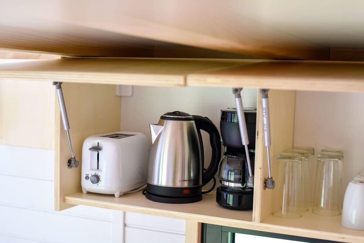 A kitchen shelf with a toaster, a kettle, a coffee maker, and several glass jars.