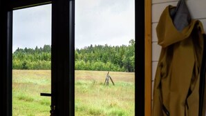 A room with a large window overlooking a grassy field and forest. - Böstebacken Tiny House by Tiny Away (Alingsås)
