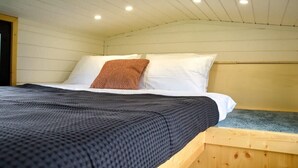 A single bed with a patterned pillow, a dark blanket, and a wooden headboard. - Böstebacken Tiny House by Tiny Away (Alingsås)