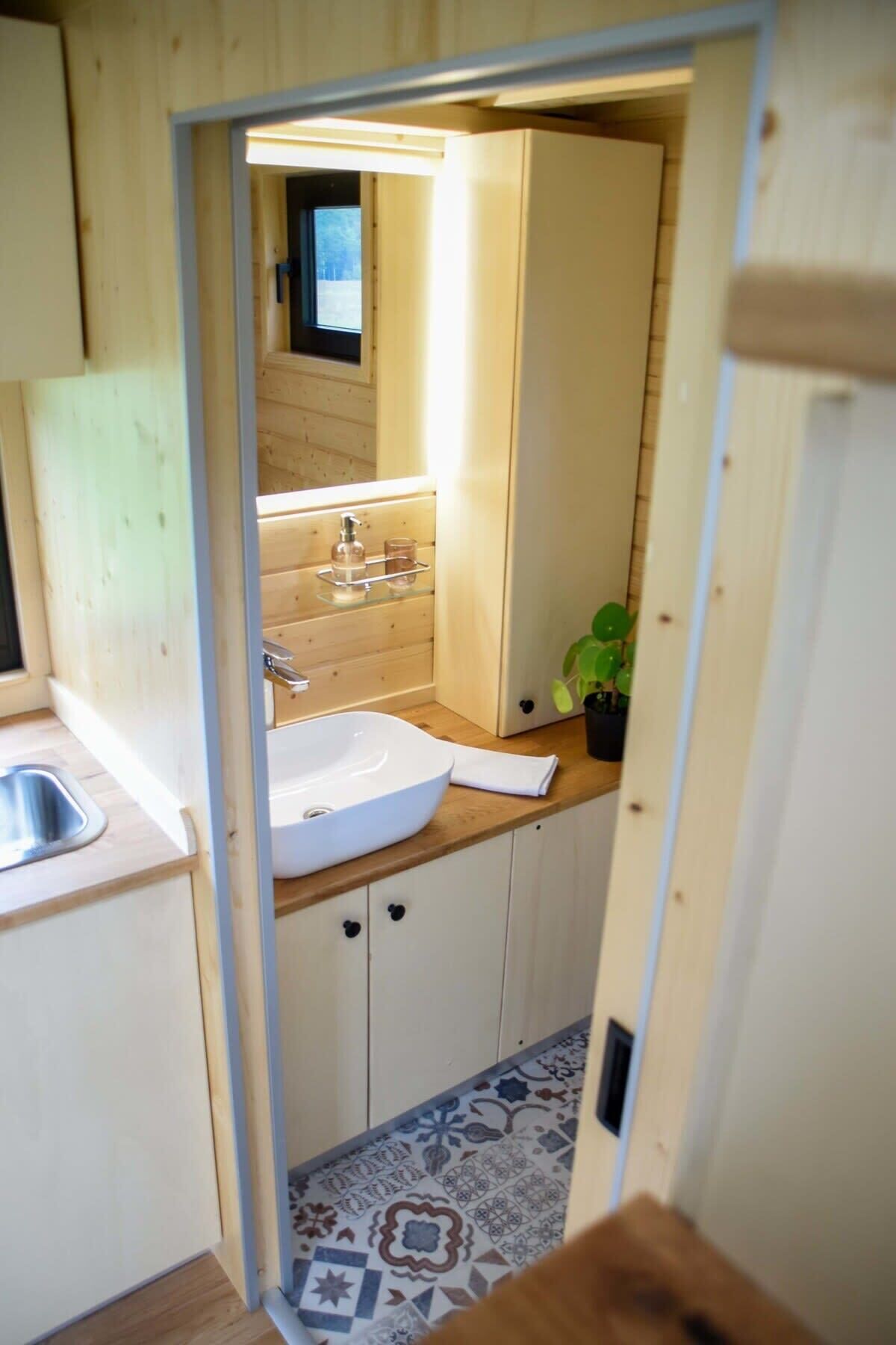 A narrow hallway leading to a bathroom with a sink, mirror, and wooden cabinets.