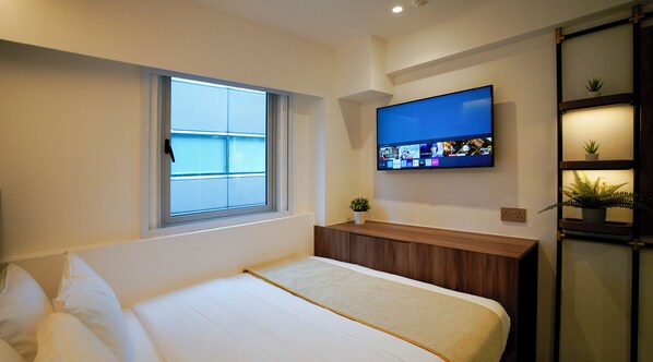 A modern bedroom with a bed, a TV mounted on the wall, a window with blinds, and a small plant on the nightstand. - ST Signature Bugis Middle, DAYUSE, 9 hours: 9AM-6PM (Singapore)
