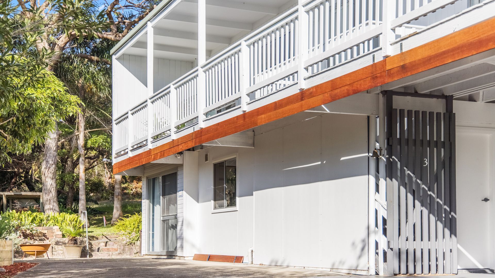 A two-story building with a white exterior, a wooden deck, and a gated entrance.
