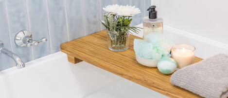 A bathroom with a wooden shelf holding a glass vase with flowers, a bottle of hand soap, a candle, and a towel.