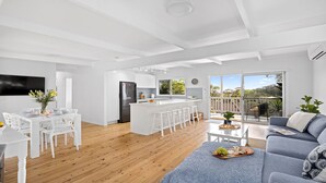 A modern kitchen with white cabinetry, a central island with bar stools, and a dining area with white chairs and a table.