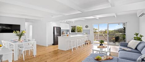 Una cocina moderna con armarios blancos, una isla central con taburetes y un comedor con sillas y mesa blancos.