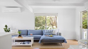 A modern living room with a grey sofa, a coffee table, and a large window with a view of trees.