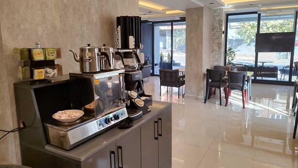 A modern coffee station with a coffee machine, a kettle, and a plate of food. There are chairs and a table in the background. - Cam Suites (Kahramanmaras)