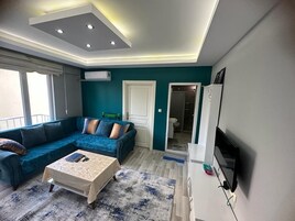 Uma sala de estar moderna com um sofá seccional, uma mesa de centro, uma TV de tela plana e um teto com iluminação embutida.