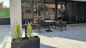 An outdoor seating area with tables and chairs, large windows, and potted plants. - Cam Suites (Kahramanmaras)