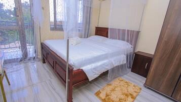 A bedroom with a wooden bed, a canopy, a wooden wardrobe, and a small rug.