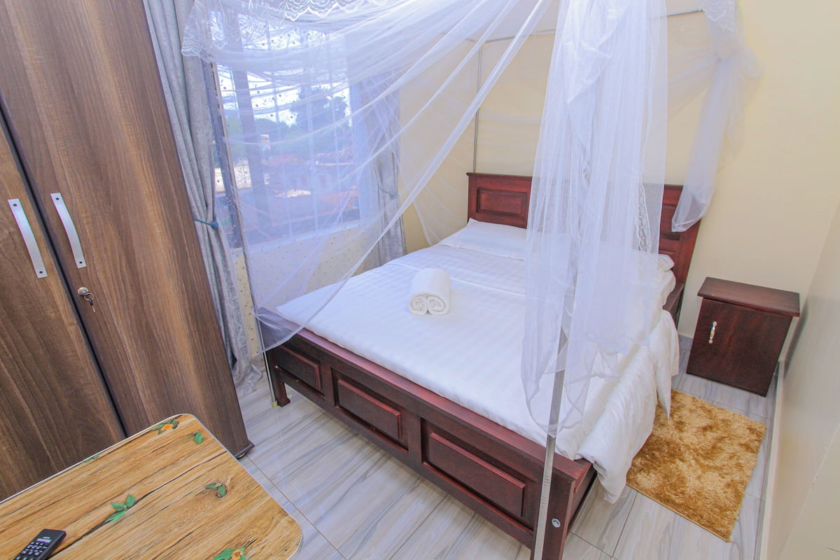 Un dormitorio con una cama de madera, una mesita de noche, un armario y una pequeña mesa con un control remoto.