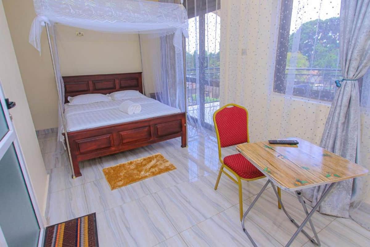 Un dormitorio con una cama de madera, una silla roja, una mesita y un ventanal con cortinas.
