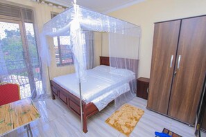 A bedroom with a four-poster bed, a wooden wardrobe, a small table, and a chair.