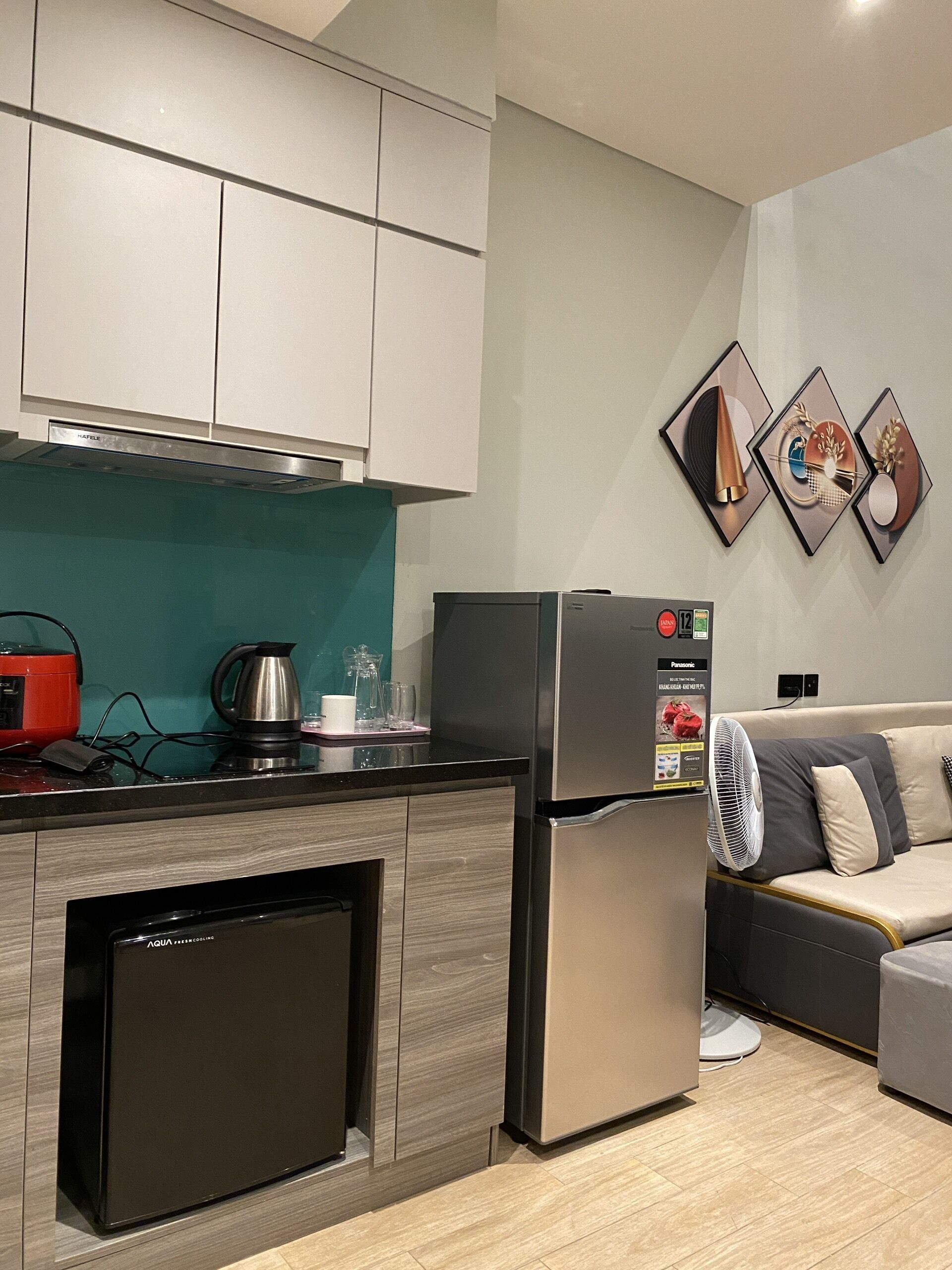 A compact kitchen with a built-in dishwasher, a refrigerator, and a small countertop with a kettle and glasses.