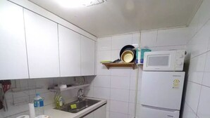 A compact kitchen with white cabinets, a microwave, a sink, and a small trash bin. - A Family House (Seoul)