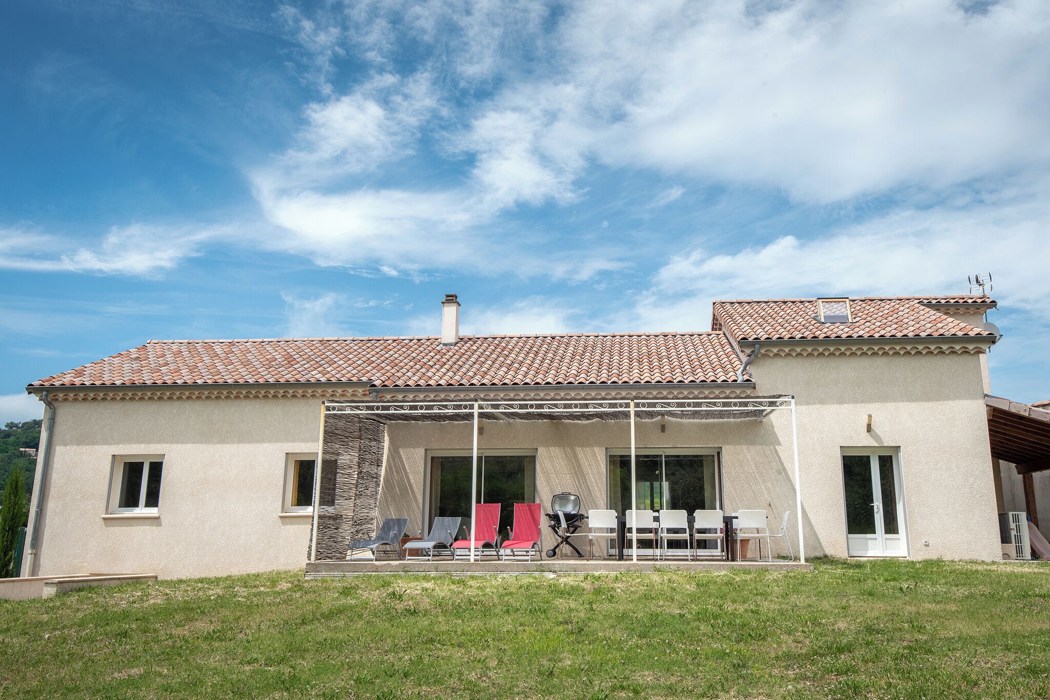 Une maison à deux étages, avec un toit en tuiles, un patio couvert doté de meubles d’extérieur et un mur en pierre.