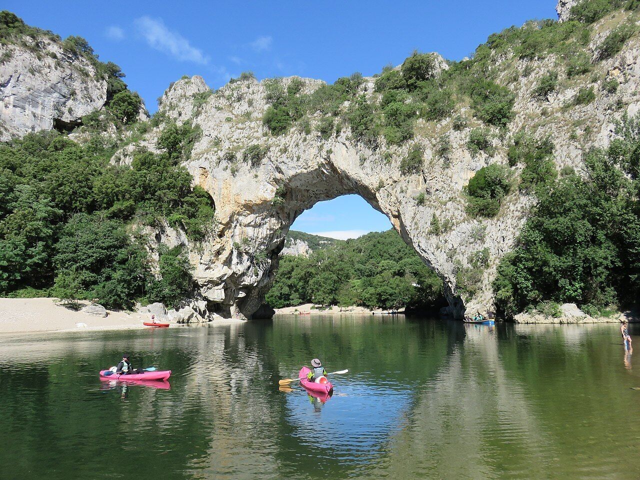 A natural rock arch formation over a calm river with kayaks.